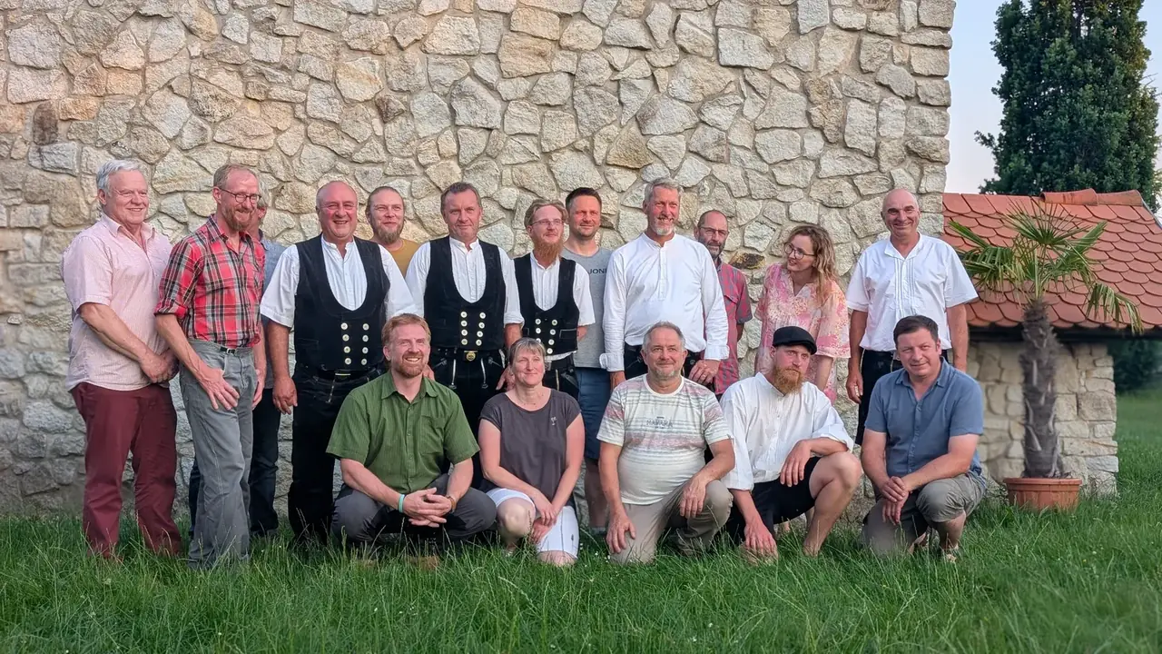 Gruppenfoto mit Zimmerern in Zunftkleidung und Gästen vor der Steinmauer